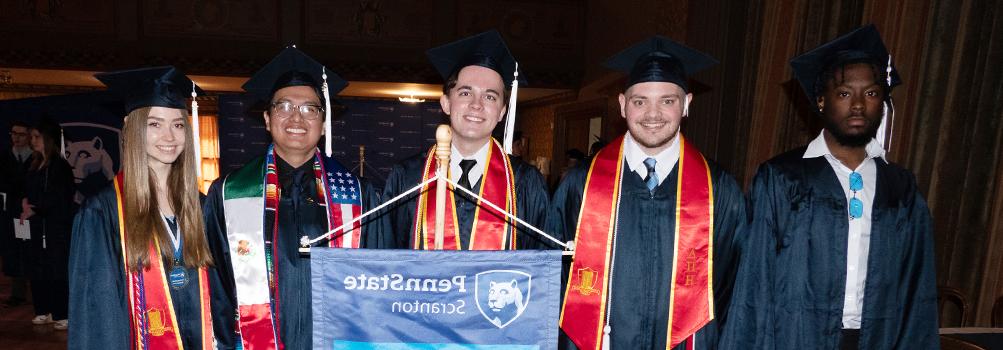 5 diverse graduates pose with penn state scranton banner 